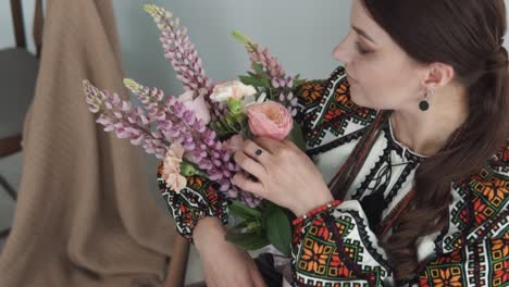 representa a una encantadora mujer joven en trajes tradicionales auténticos ucranianos sosteniendo un gran y hermoso ramo de flores y sonriendo a la cámara