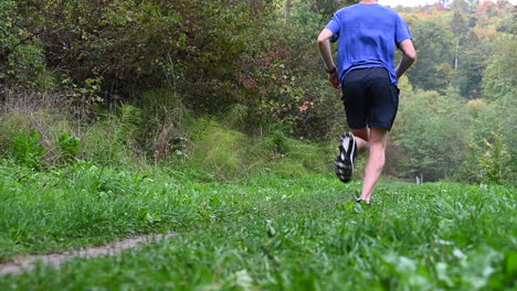 Cámara-Lenta,-Un-Joven-Atleta-Con-Una-Camiseta-Azul-Corre-En-La-Naturaleza,-Terneros-Definidos