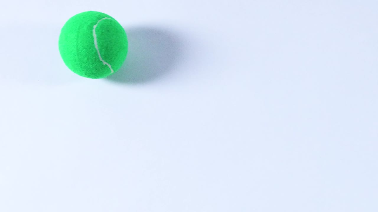 A green tennis ball rolls across a plain white background, showcasing its movement and texture.