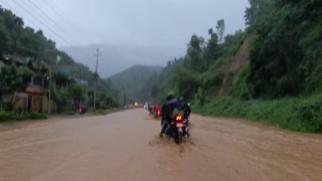 motocicletas circulando por una carretera inundada por aguas pluviales muy turbias durante un tifón en nepal