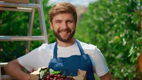 Smiling-garden-worker-carrying-cherry-crate-in-natural-agricultural-plantation