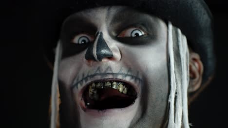 Man-with-skeleton-makeup-trying-to-scare,-opening-his-mouth-and-showing-dirty-black-teeth-and-tongue