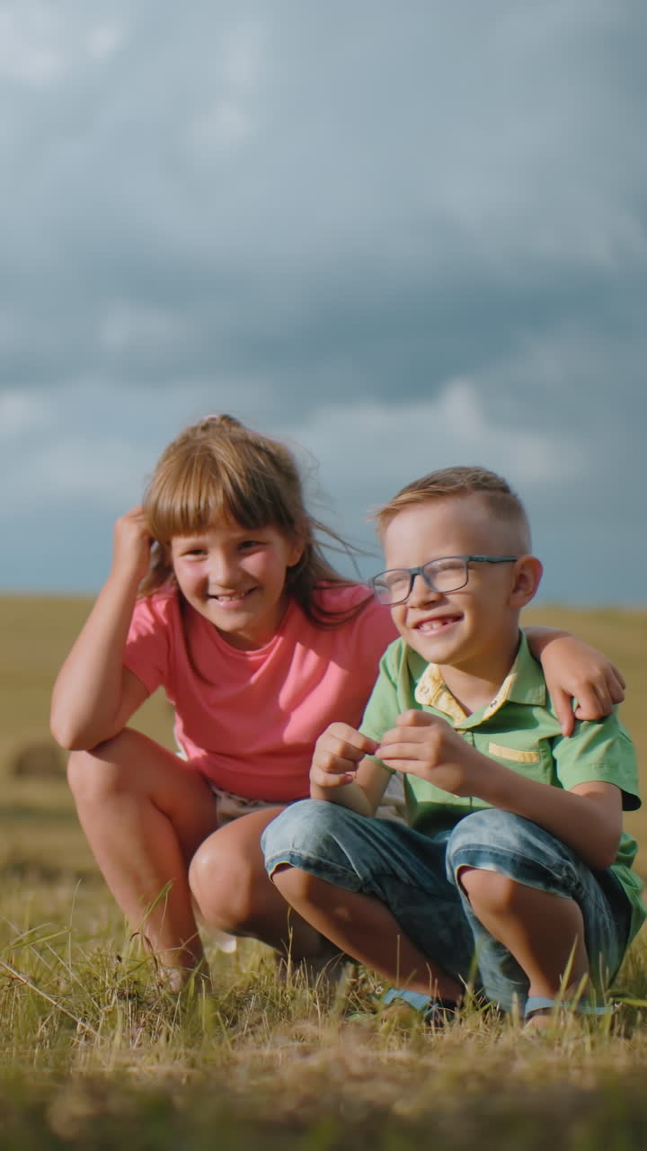 Fratello e sorella accovacciati all'aperto sotto la luce dorata del sole, sorridono mentre posano per una foto, la sorella tiene affettuosamente il fratello mentre la madre cattura il commovente momento fraterno.