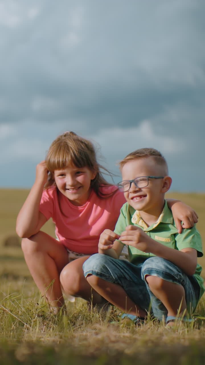 Fratello e sorella accovacciati all'aperto sotto la luce dorata del sole, sorridono mentre posano per una foto, la sorella tiene affettuosamente il fratello mentre la madre cattura il commovente momento fraterno.