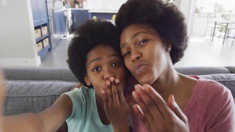 happy african american mother and daughter sitting on sofa using smartphone, taking selfie