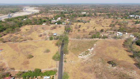 Lineare-Schwarze-Asphaltstraße-Mit-Großen-Villen-Mit-Einem-Pool-In-Der-Trockenen-Umgebung-Von-Yopal-Mit-Dem-Trockenen-Fluss-Rio-Cravo-Sur-Im-Hintergrund