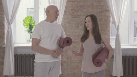 viejo hombre y mujer hablando con una alfombra de yoga en casa