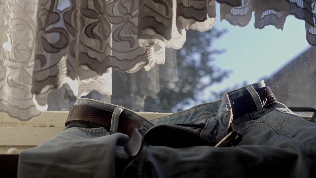 Casual denim jeans hang on warm radiator under bedroom curtain window