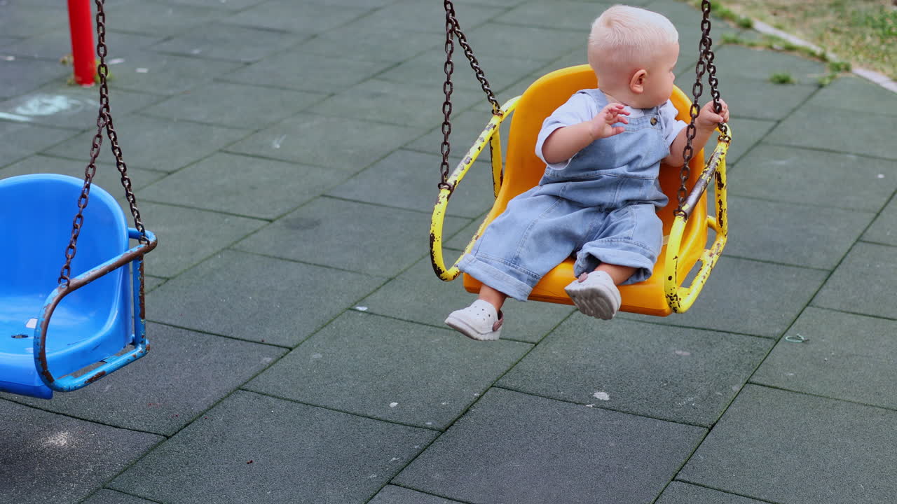 Toddler boy playing on playground in summer under the sun. Child playing in kindergarten yard. Active child on colorful swing. Healthy summer activity for kids. Little boy swinging