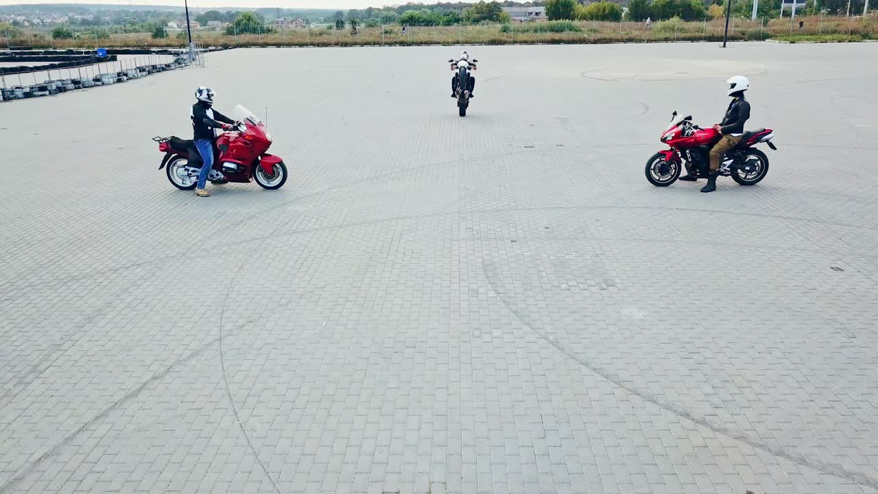 Professional motobiker is riding on one wheel on a high speed on the background of two other bikers. Men in special clothes and helmets driving sport motorcycles on a racing track outdoors.