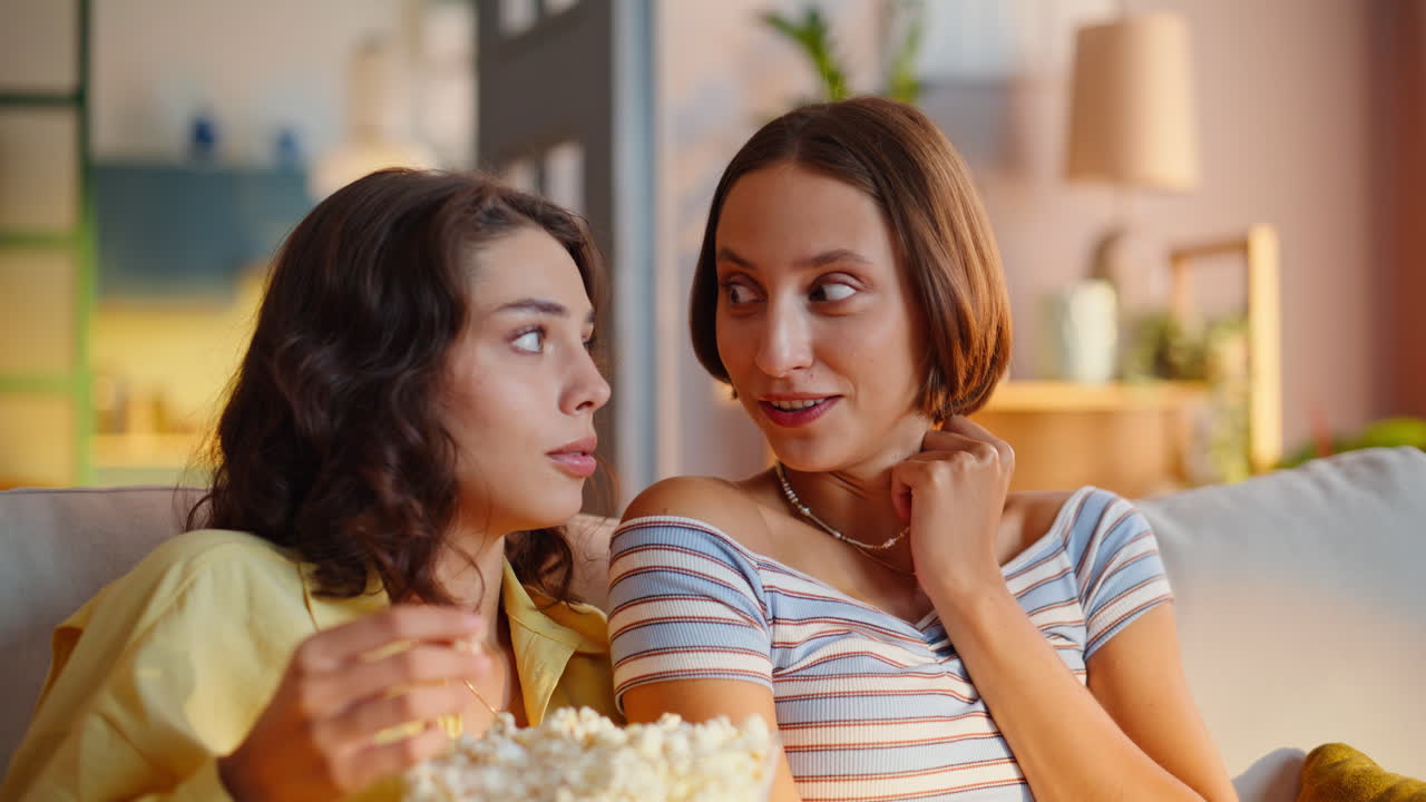 To kvinder ser spændende thriller på TV og sidder tæt sammen på en behagelig sofa, nærbillede