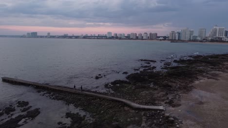 Couple-walking-along-pier-on-cloudy-day-with