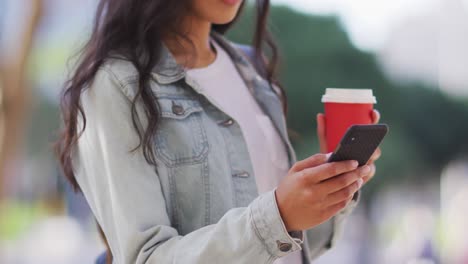 mujer asiática usando un teléfono inteligente y sosteniendo café para llevar