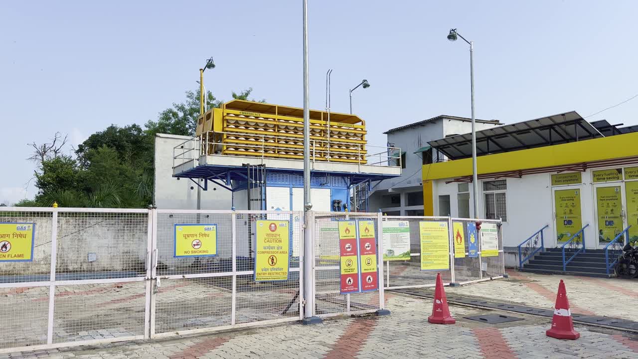 Tilt-up shot of a CNG (compressed natural gas) station with storage cylinders, safety signs, and refueling facility under daylight