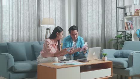 asian couple with a laptop holding the bill and credit card using smartphone spending money