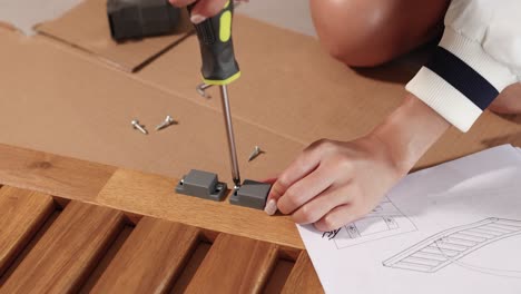 a person uses a screwdriver to assemble furniture, following instructions. bright lighting highlights the detailed process