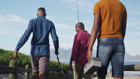 Padre-Mayor-Afroamericano-Y-Dos-Hijos-Adolescentes-Parados-En-Una-Playa-Pescando-Y-Hablando