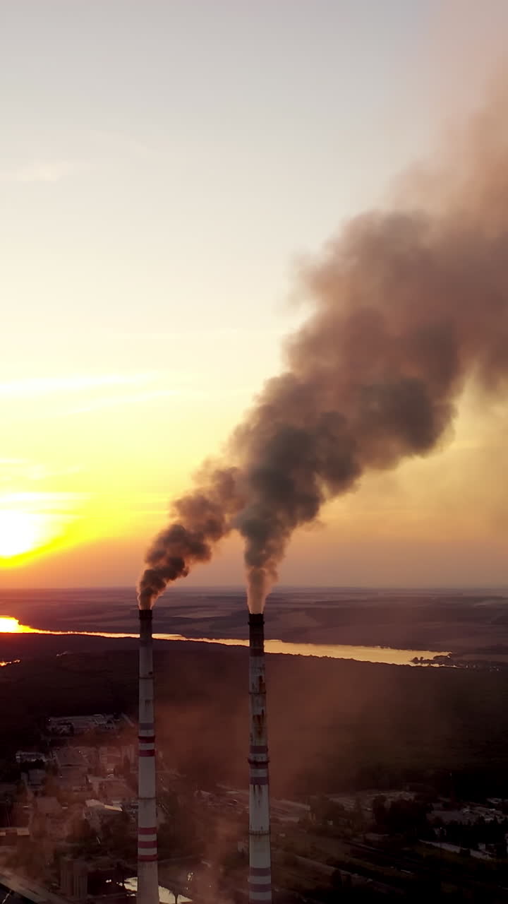 Industrial factory at sunset. Dirty smoke coming from pipes on the nature background in the evening. Manufacture near the river. Vertical video