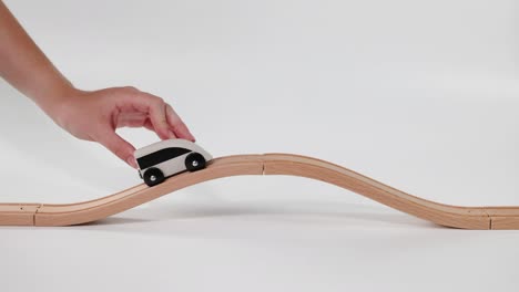 hand moves toy car on wavy wooden track