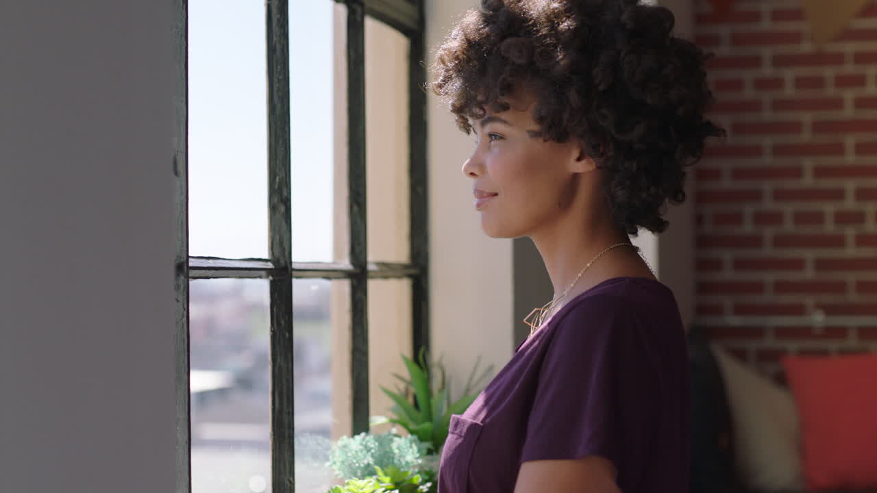 donna afroamericana felice che usa lo smartphone a casa, naviga i messaggi, gode di uno stile di vita rilassato, guarda fuori dalla finestra, pianifica in anticipo, donna nera che manda messaggi sul cellulare