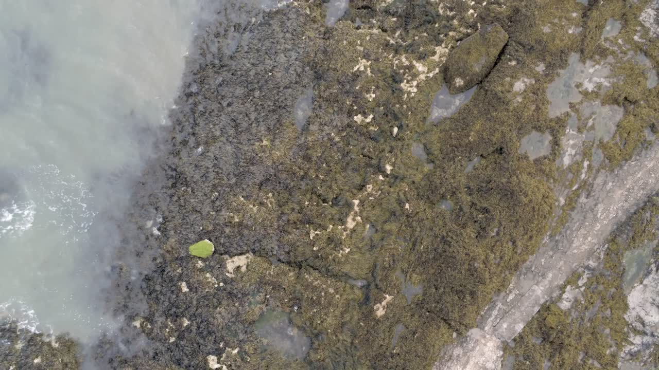 Aerial rising birdseye view above rocky seaweed coast rock pool landscape