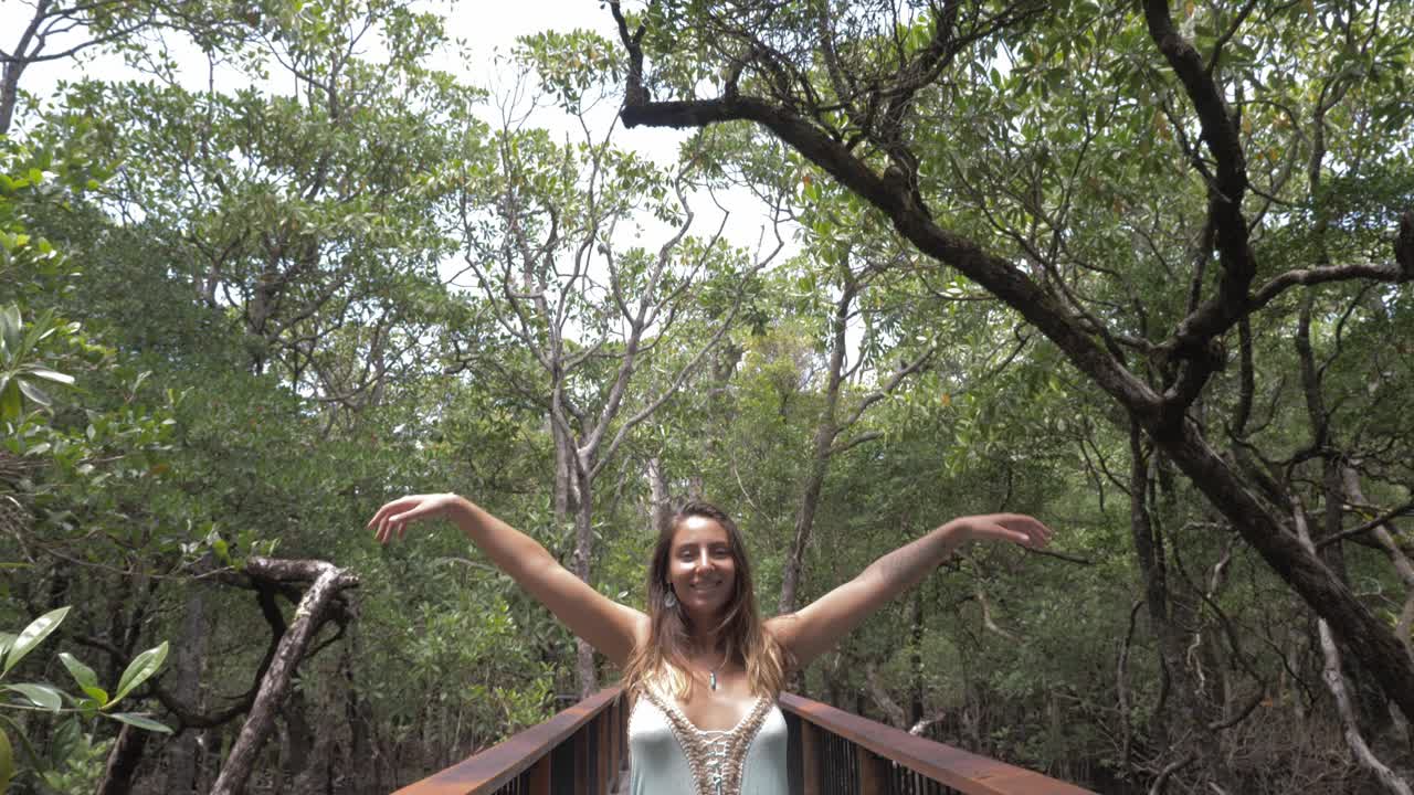dama sexy con vestido, levanta los brazos mientras está de pie en la pasarela de acero en la selva tropical de daintree, queensland, australia