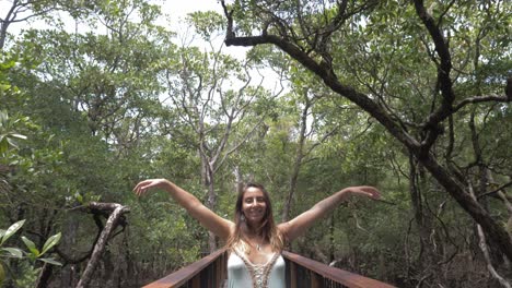 Dama-Sexy-Con-Vestido,-Levanta-Los-Brazos-Mientras-Está-De-Pie-En-La-Pasarela-De-Acero-En-La-Selva-Tropical-De-Daintree,-Queensland,-Australia