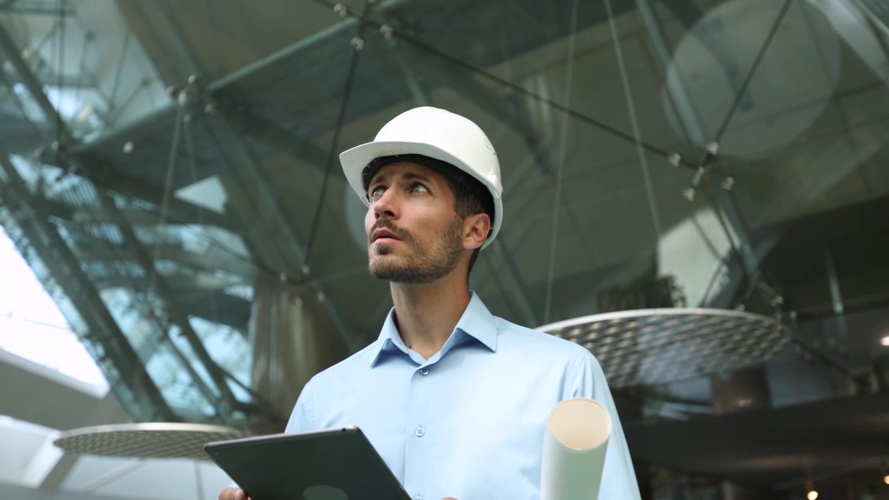 Ingeniero con casco usando una tableta y planos en un edificio moderno
