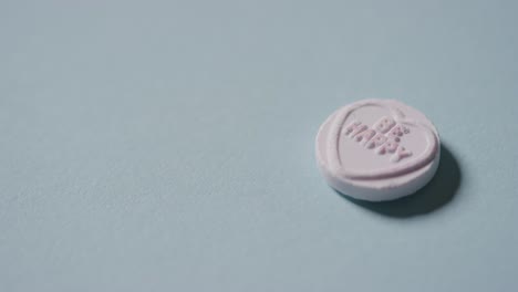 Hand-Picking-Up-Heart-Candy-With-Romantic-Message-Be-Happy-On-Blue-Background