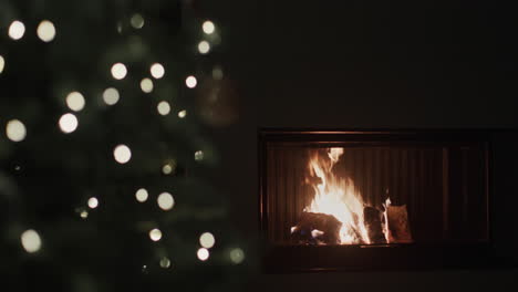 a fire burns in a fireplace in a dark room. blurred christmas tree lights in the foreground