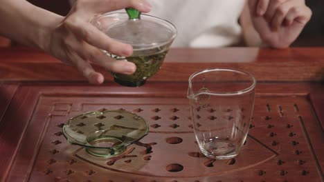 pouring infused green tea from gaiwan into the glass on traditional dark wood tea table