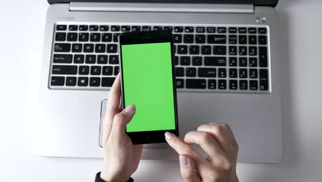 las manos femeninas tocan la pantalla táctil del teléfono inteligente. pantalla verde, concepto chromakey, portátil en el fondo. top shot 60 fps