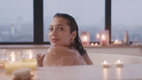 vista trasera de una mujer bañándose en una bañera y mirando hacia atrás