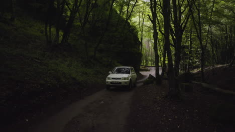 Toma-Aérea-Suave-De-La-Parte-Delantera-De-Un-Todoterreno-Conduciendo-Cuesta-Arriba-A-Través-De-Un-Bosque-Tranquilo