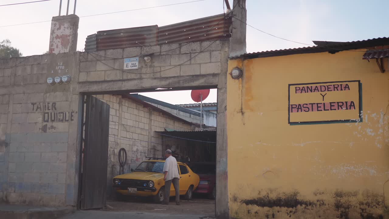 Interesting colourful composition of a man washing his yellow car in his street front garage, contrasting with the yellow walls outside his property