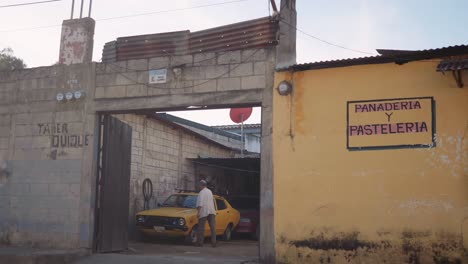 interesante composición colorida de un hombre lavando su auto amarillo en su garaje frente a la calle, contrastando con las paredes amarillas fuera de su propiedad