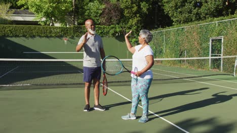 african american senior couple holding rackets high fiving each other on the tennis court