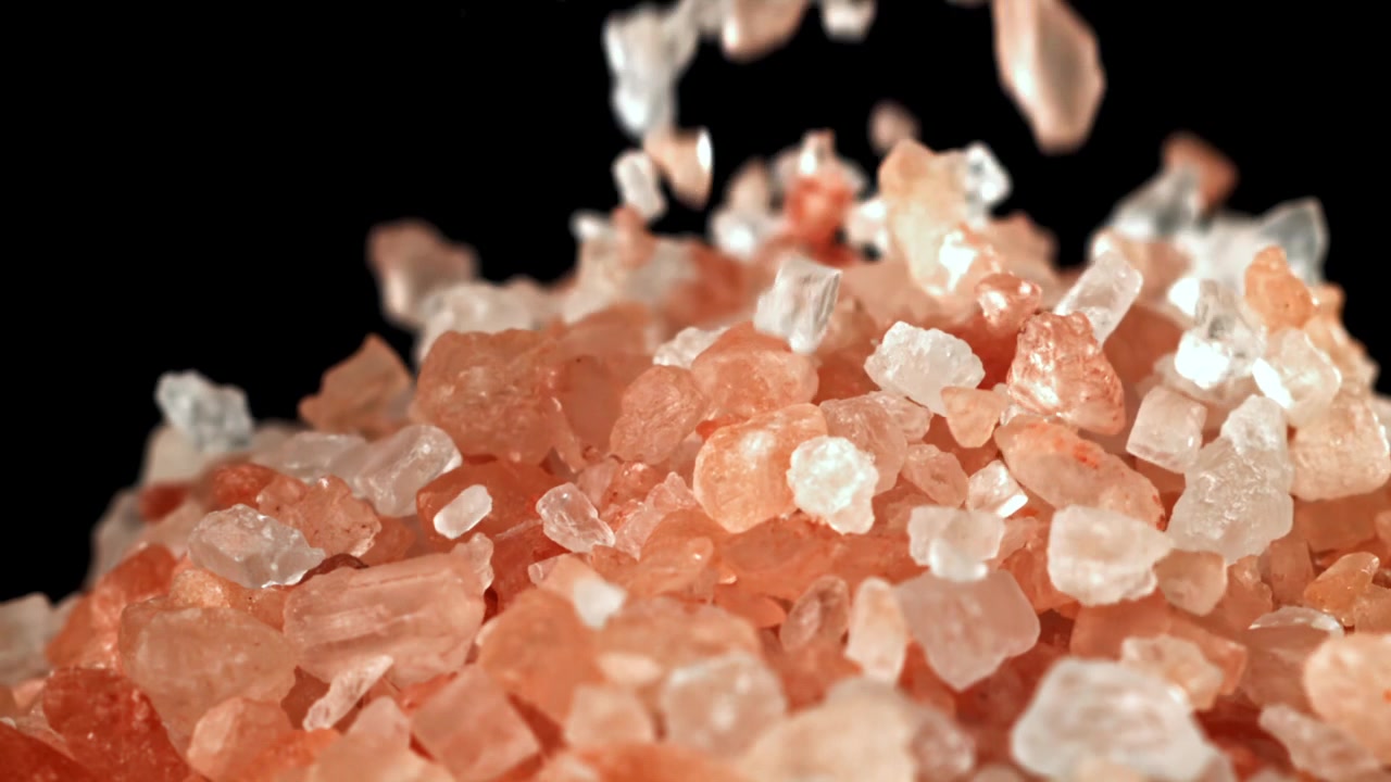 Cristalli di sale rosa dell'Himalaya che cadono su sfondo nero al rallentatore