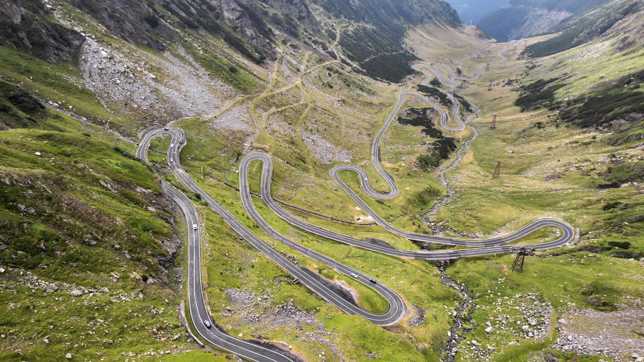 Aerial drone view of nature in Romania. Transfagarasan route in Carpathian mountains with moving cars, rocky slopes with greenery