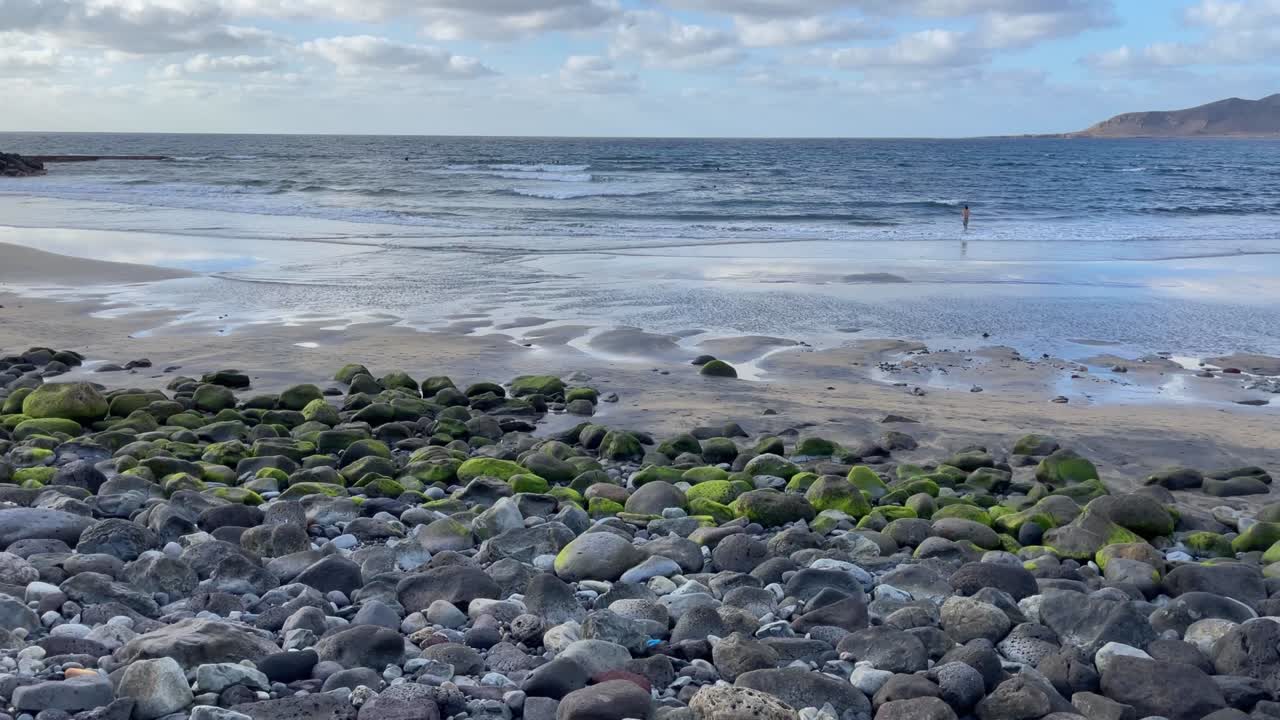 시세르 해변의 바위와 라스 팔마스 시의 파도를 타는 서퍼들