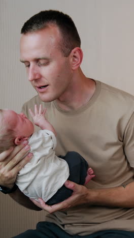 caucasian male wearing beige t-shirt waving his baby. newborn is crying and waving tiny hands. vertical video