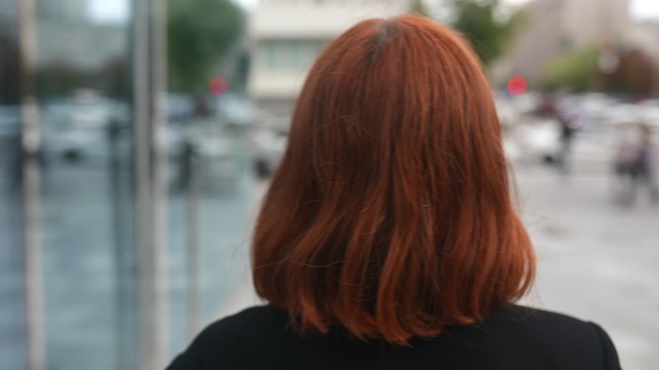 빨간 머리카락을 가진 여자가 도시에서 멀리보고 있습니다.