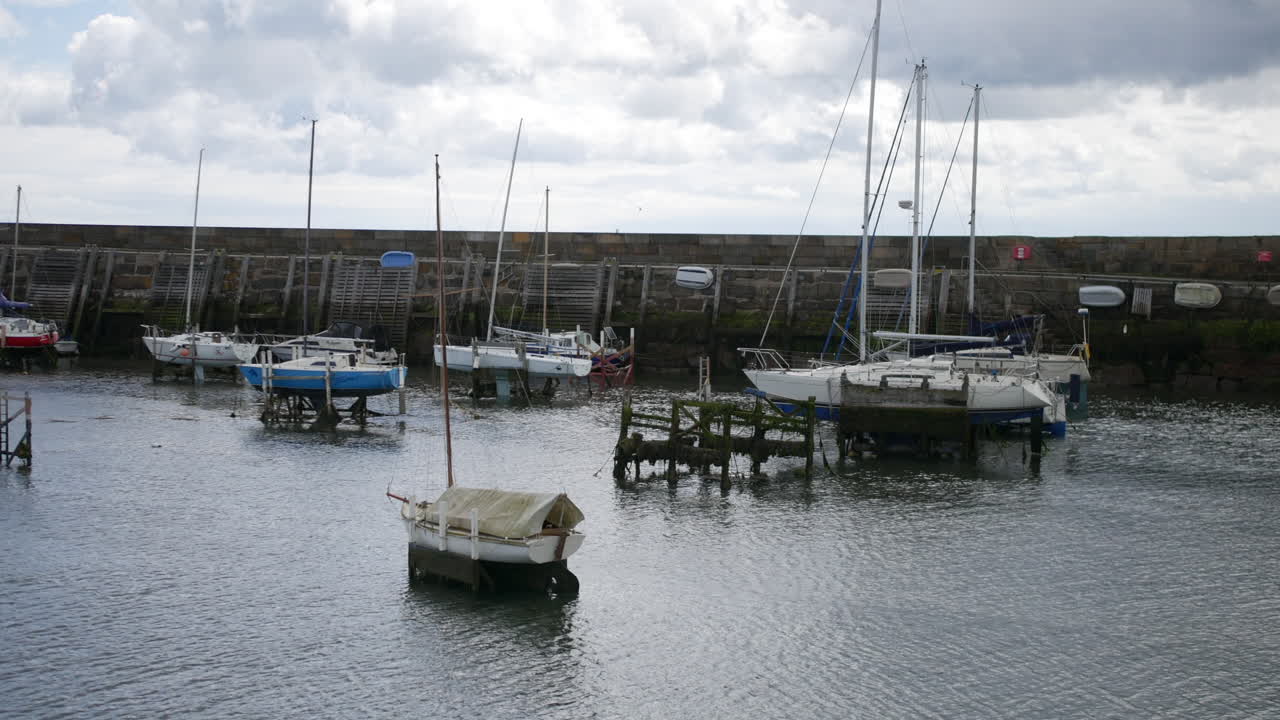 Boats rest in the harbor at Scarborough, North Yorkshire, England, with small yachts and wooden piers standing in calm water beside a stone seawall
