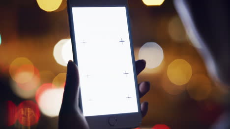 persona sosteniendo un teléfono inteligente por la noche con una pantalla en blanco