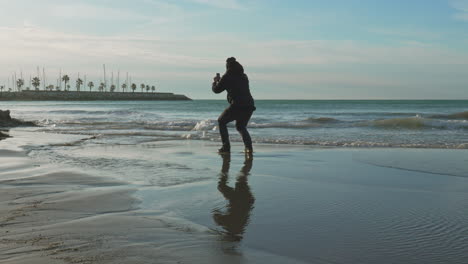 Man-takes-a-photo-of-sunset-on-a-beach,-with-waves-low-tide-wet-sand