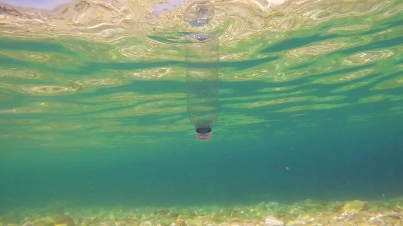 En plastikflaske ses flyde under vandet i havet. Vandoverfladen reflekterer lys. Dette billede viser plastikforureningens indvirkning på havmiljøet.