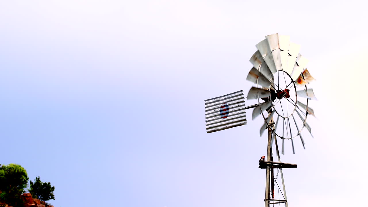 Old rusty windmill spinning in wind pumping up water on farm, slow motion