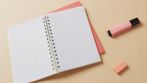 Overhead view of open notebook with school stationery on beige background, in slow motion