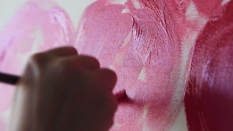 Close-up-of-unrecognizable-artist-paints-red-peonies-or-other-flowers-with-brush-on-the-canvas.-The-artist-paints-pink-flowers-on-canvas-with-thick-brush,-close-up,-side-view