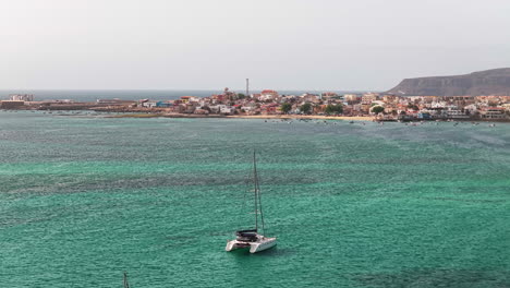 Nice drone view of the city of Sal Rei, luxury yacht moored in turquoise ocean, background the port, its old color city and the desert with the mountains